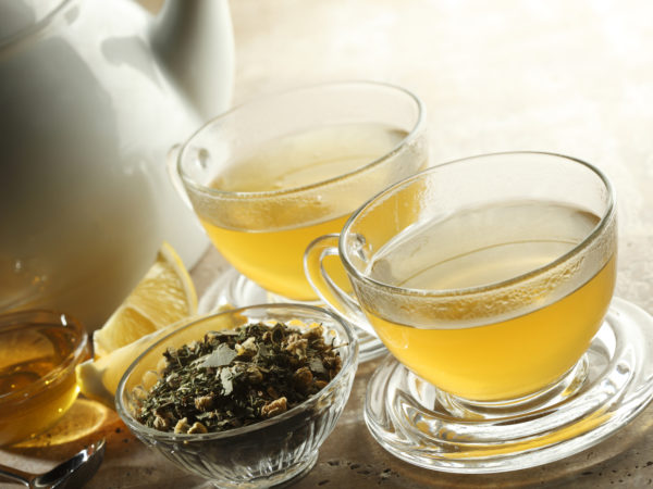 "Two glasses of tea. Teapot,honey, lemon, and loose tea beside cups."