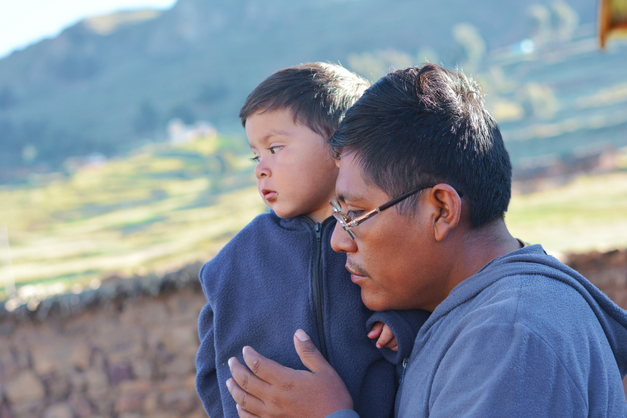 A father hugs his son while standing outside. Both are looking down.